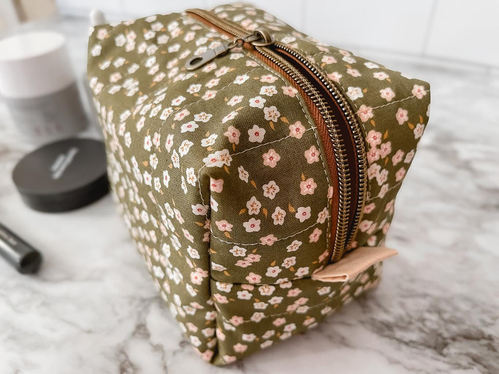 Floral-patterned toiletry bag on a marble surface with makeup items.
