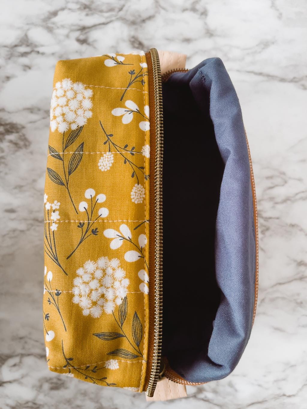 Yellow floral-patterned pouch with a blue interior on a marble surface