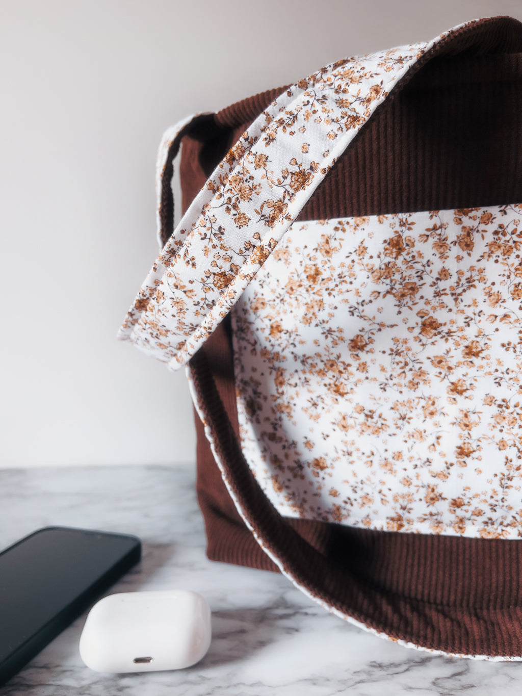 Floral-patterned front slip pocket on brown corduroy exterior fabric mini tote bag with a phone and white air pods case on a marble surface