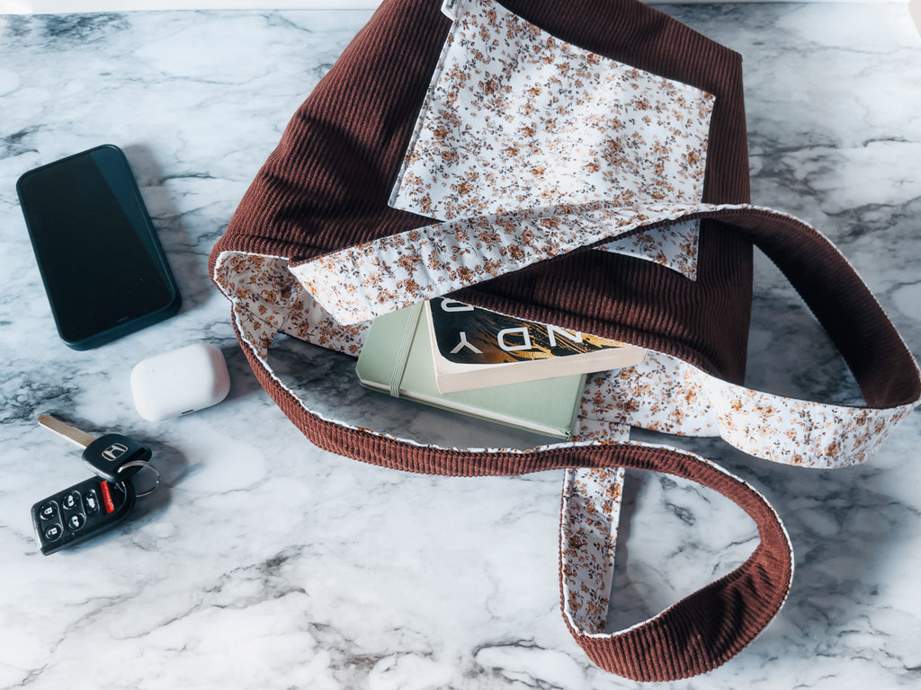 Floral-patterned front slip pocket on corduroy exterior fabric and floral interior lining mini tote bag with phone, keys, and wallet on a marble surface