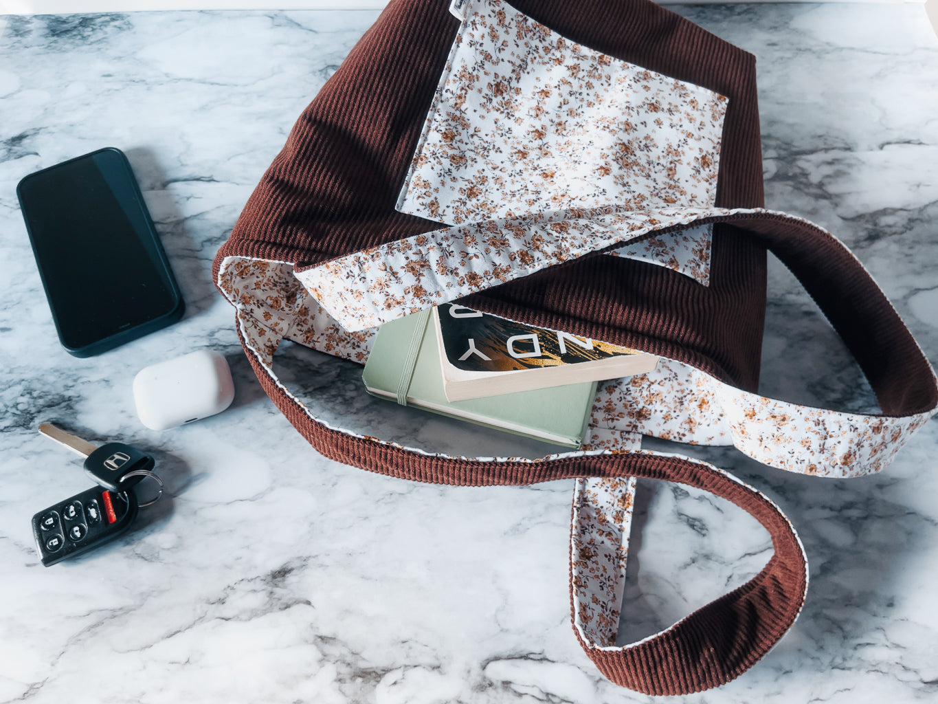 Floral-patterned front slip pocket on corduroy exterior fabric and floral interior lining mini tote bag with phone, keys, and wallet on a marble surface
