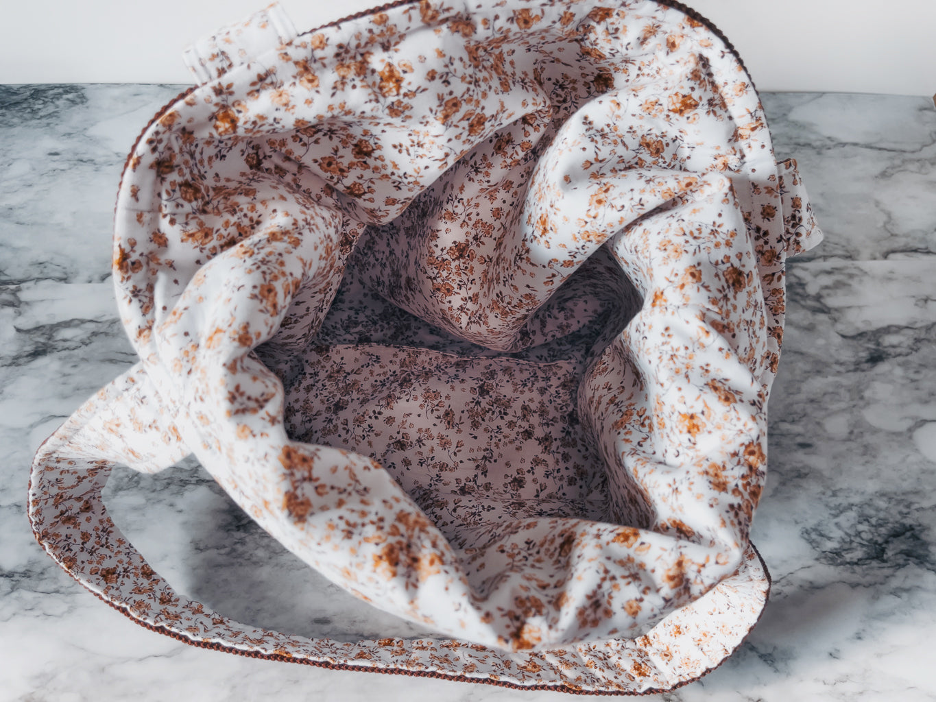 Plush fabric lining with brown floral design mini tote on a marble surface