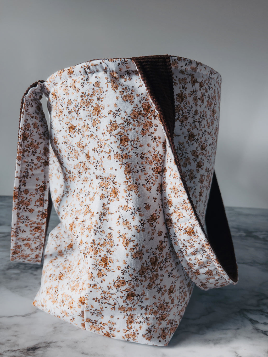 Floral-patterned fabric mini tote turned inside out with multi fabric straps hanging over a surface with a neutral background