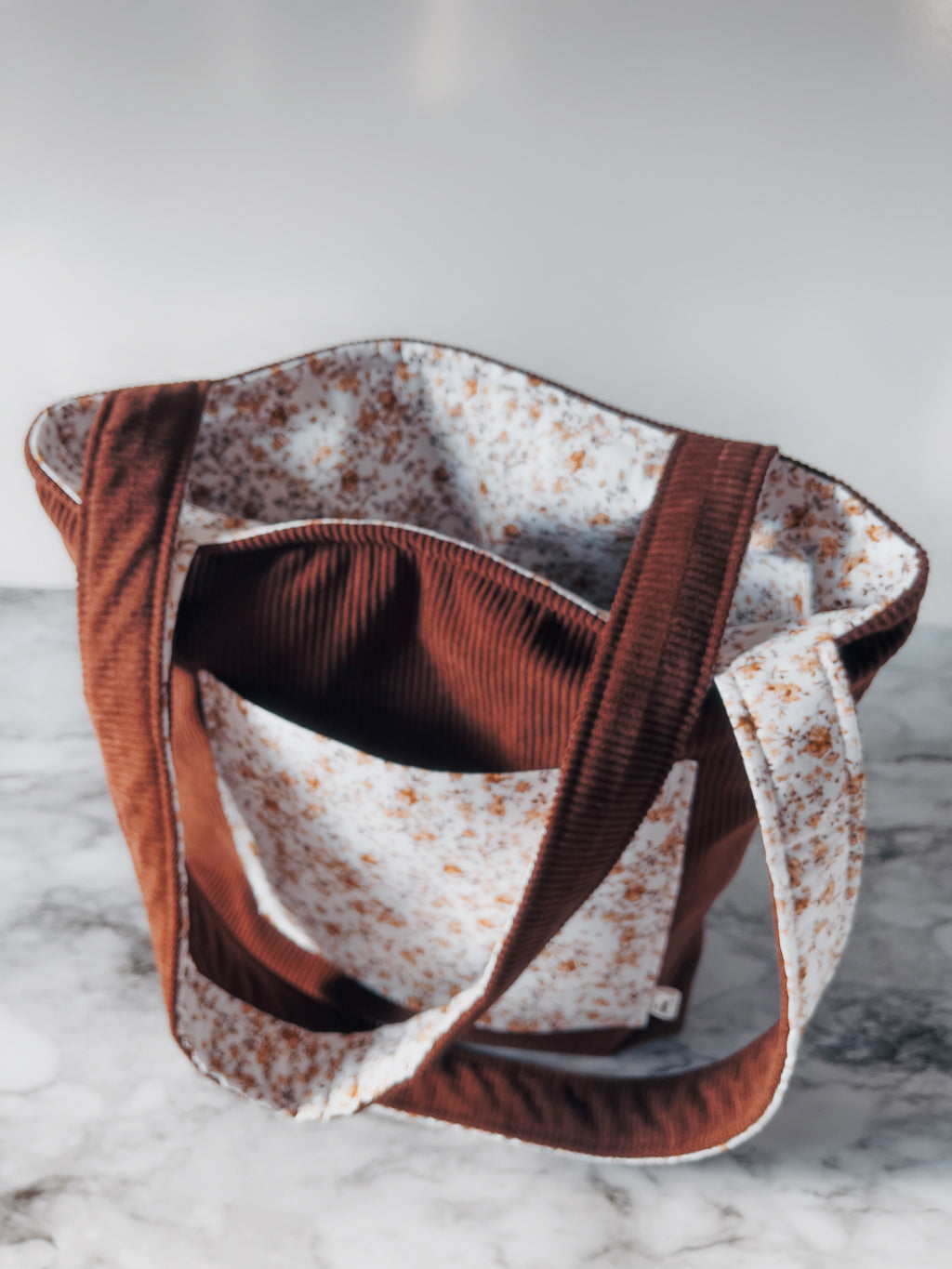 Brown corduroy fabric bag with floral interior on a marble surface