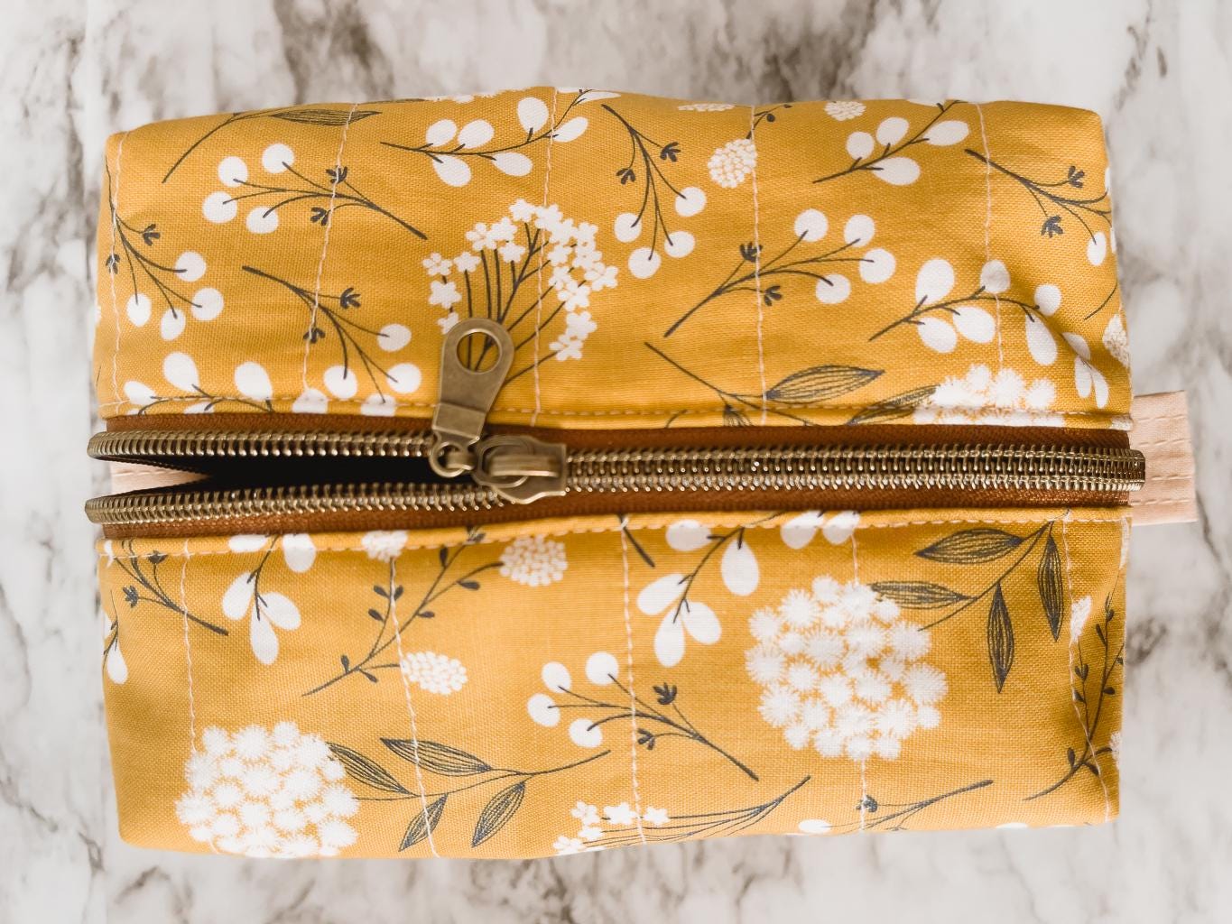 Floral-patterned pouch with a gold zipper on a marble surface