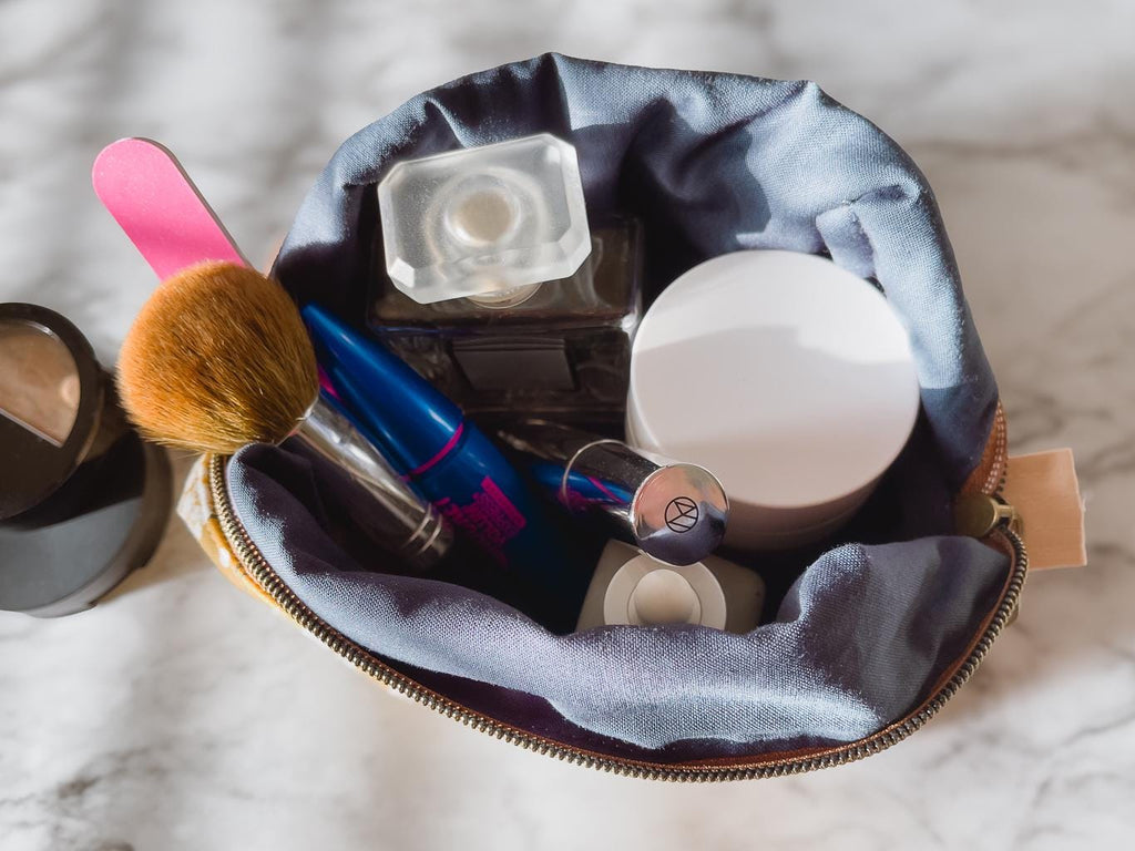 Makeup bag with various cosmetic items on a marble surface