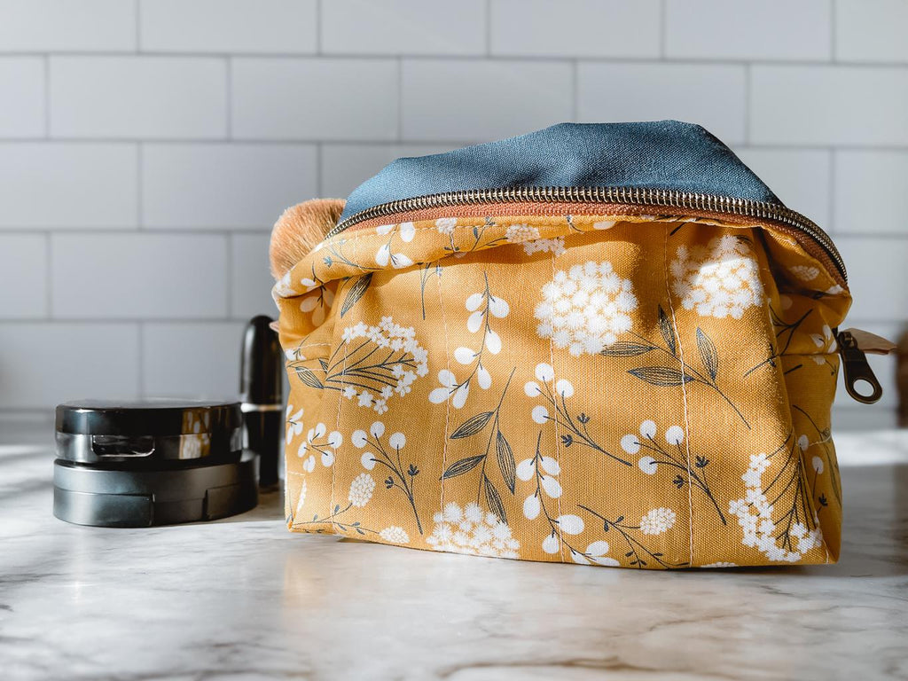 Yellow floral-patterned makeup bag on a marble surface with a white tiled wall background