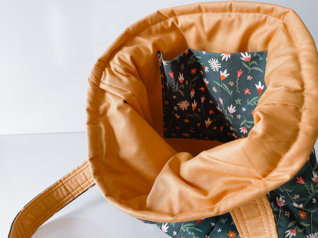 Close-up of a tan fabric bag with a floral patterned interior slip pocket on a white background