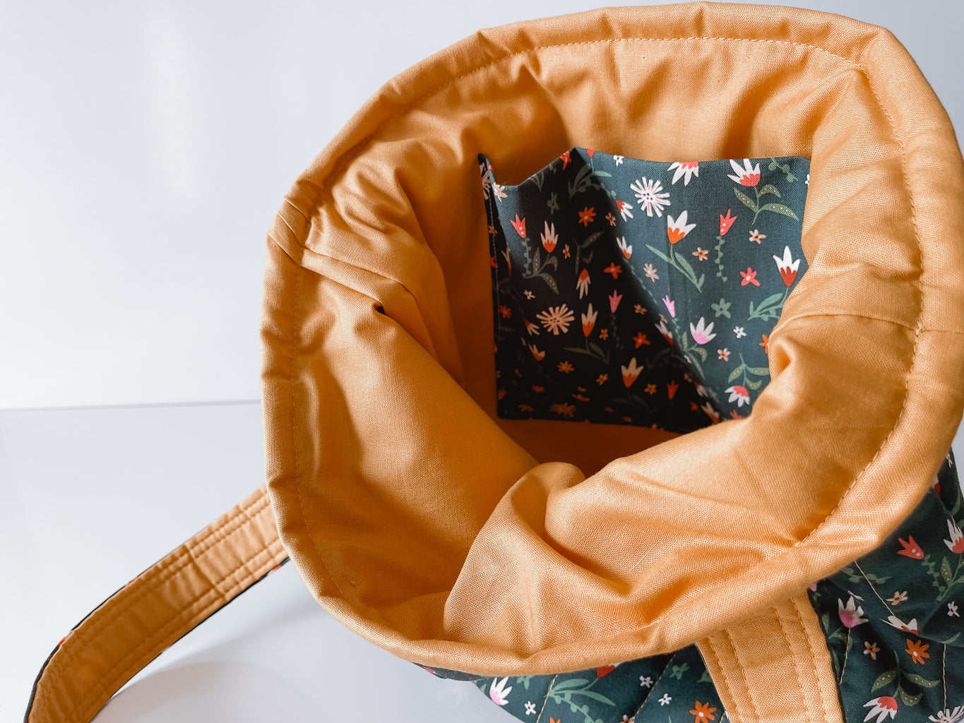 Close-up of a tan fabric bag with a floral patterned interior slip pocket on a white background