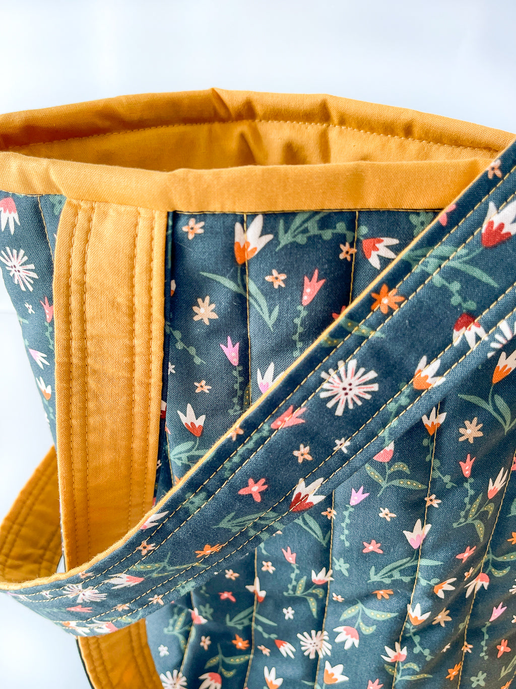 Close-up of a floral-patterned fabric on forest green with yellow interior lining on a white background