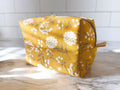 Yellow floral-patterned pouch on a marble surface with a tiled wall background