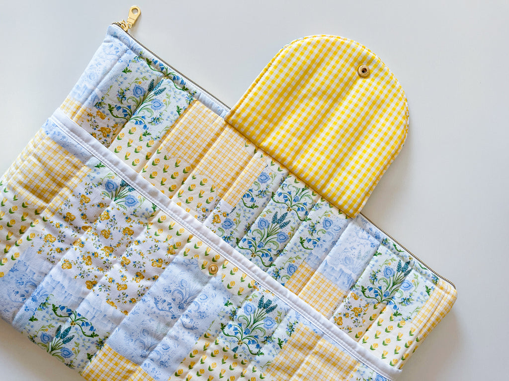 Patchwork print laptop sleeve with floral and gingham patterns on a light background