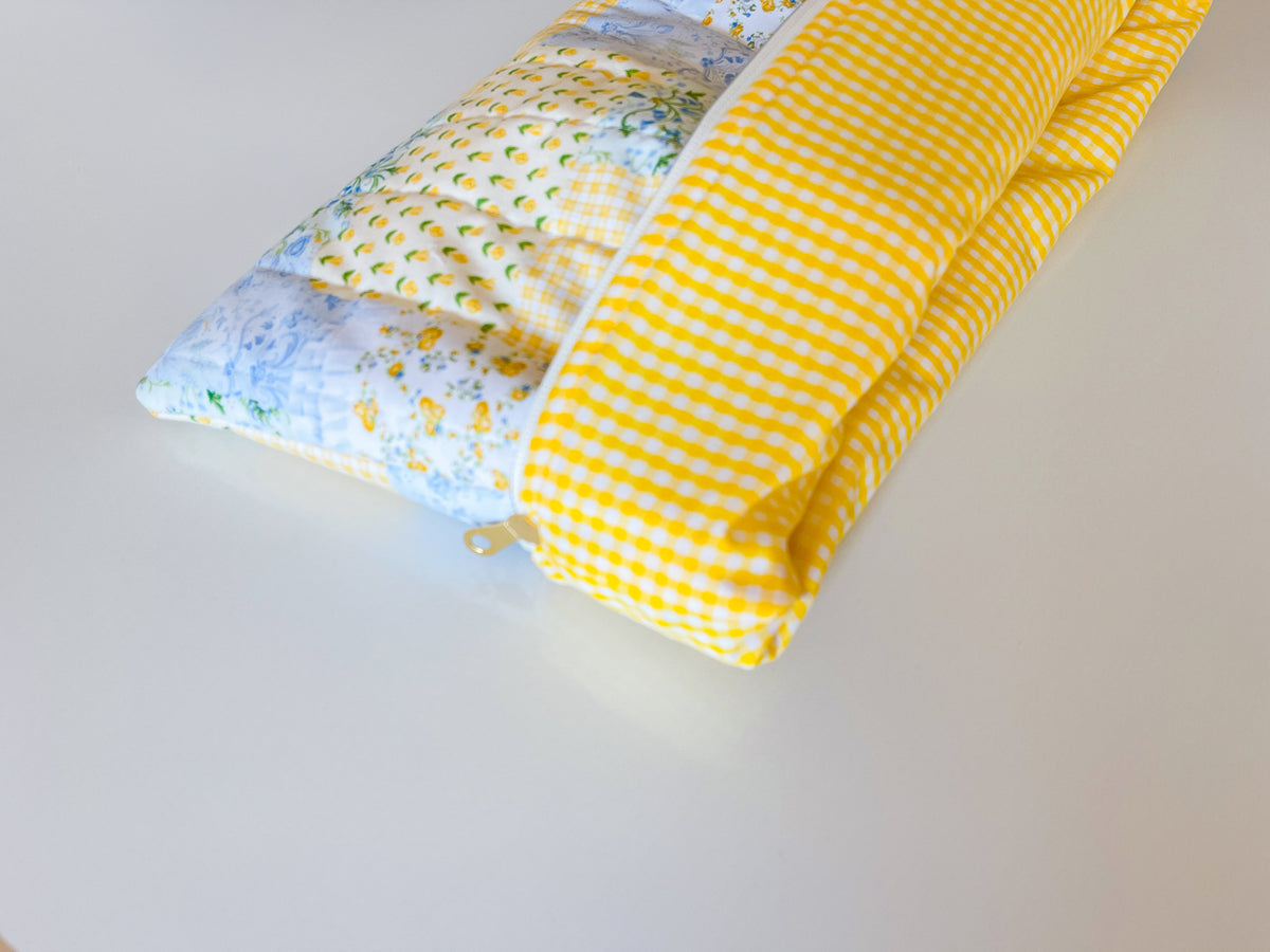 Laptop sleeve folded halfway showing inside yellow white gingham lining fabric with patchwork print exterior quilted blue green and yellow with floral tulips
