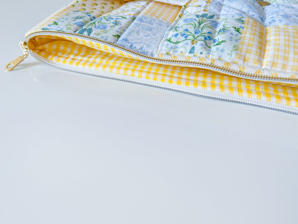 Patchwork-style laptop sleeve with floral patterns and a yellow border on a light gray background zipper with gold pull and yellow white gingham inner lining